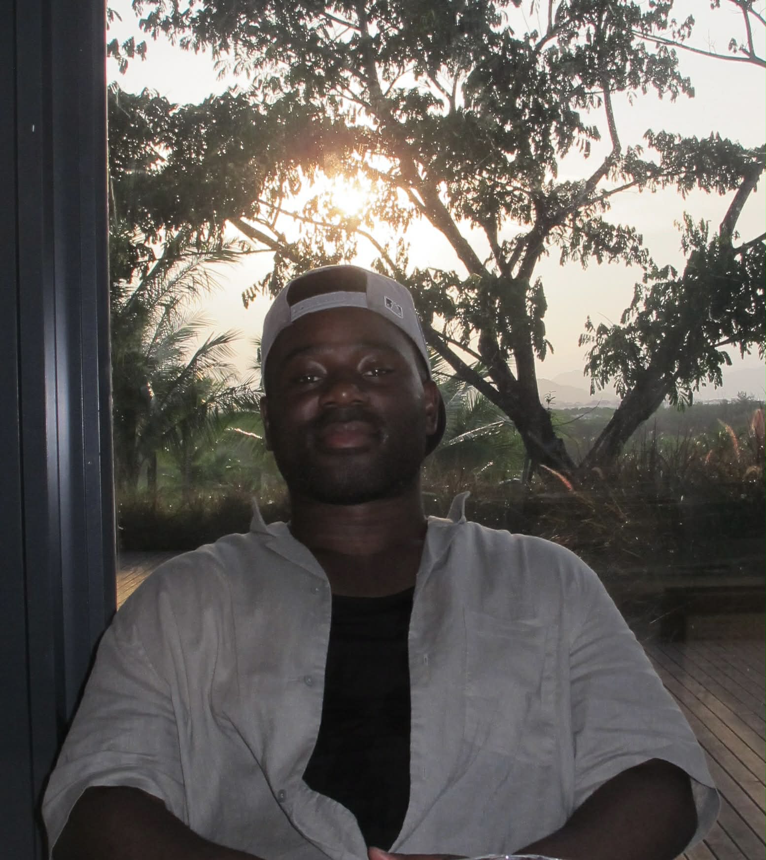 Man posing confidently in a stylish neutral outfit at a tropical outdoor location with bamboo and palm trees.