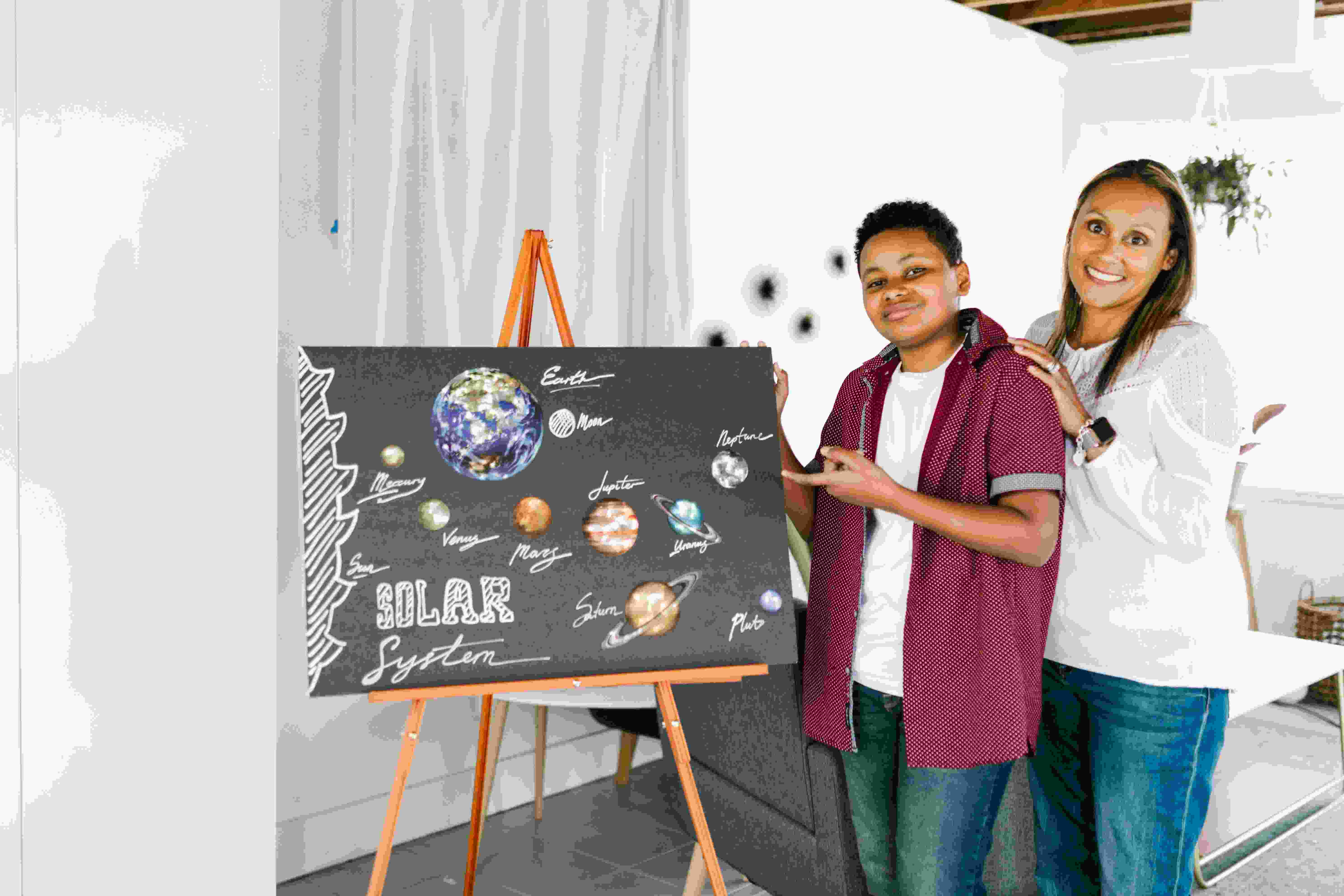 Two people standing close to eachother by a teachers board that has the solar system drawn on it 
