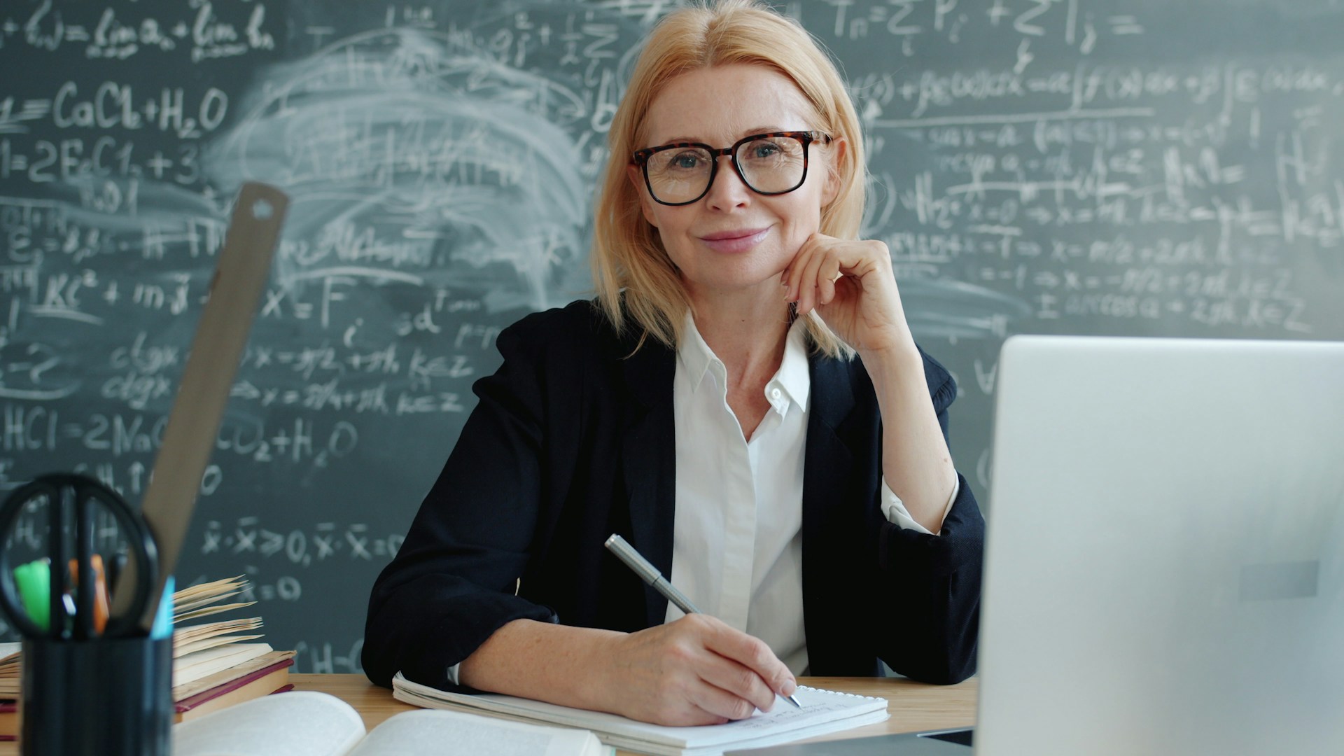 Person at desk writing with chalkboard full of equations