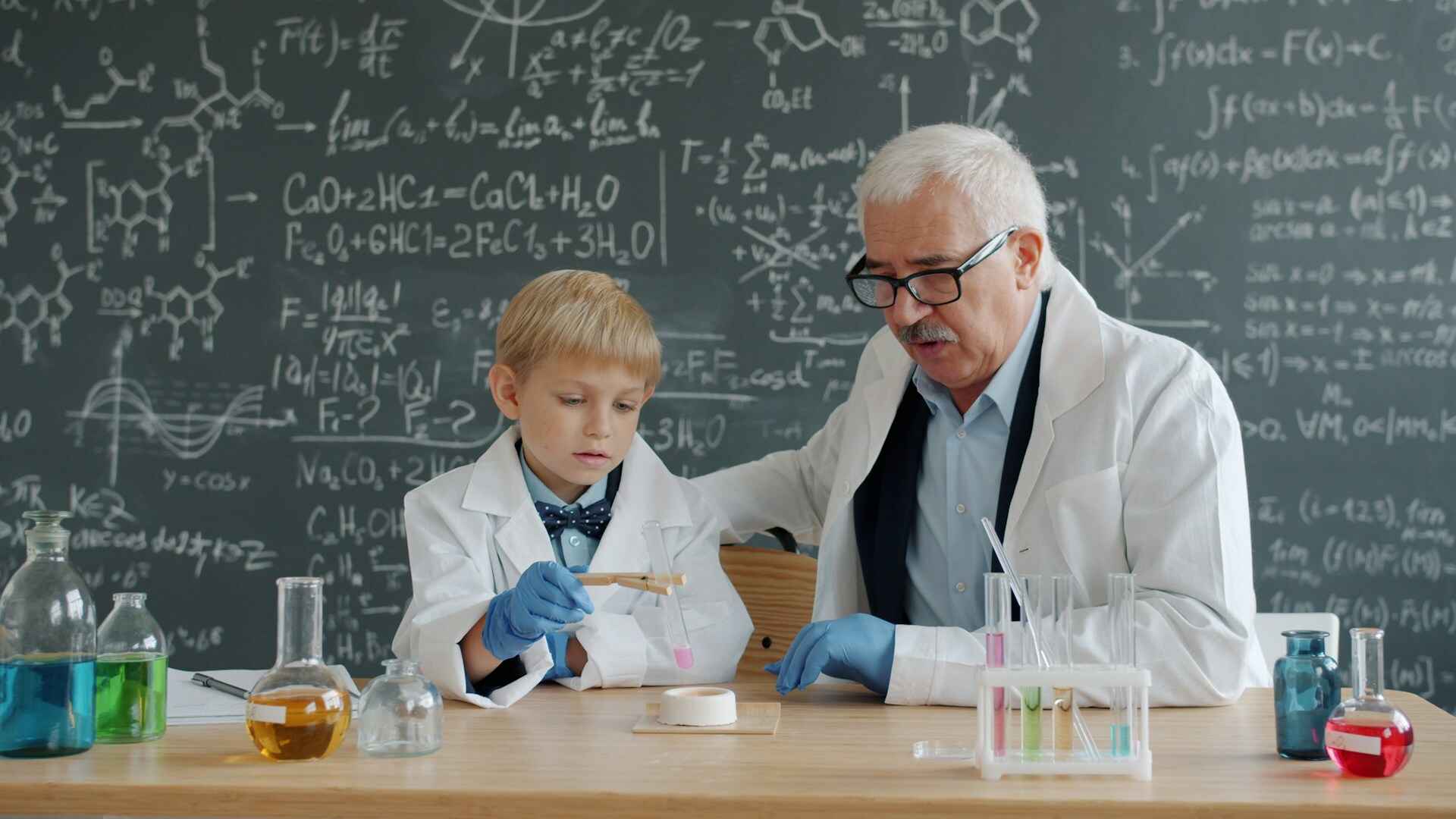 Teacher and young student sitting in lab coats expirementing in the classroom